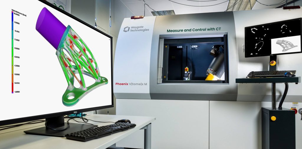 实验室中Waygate Technologies Phoenix VTomelx M CT机器的照片,显示屏上展示扫描对象的3D彩色模型,桌上有键盘和鼠标。