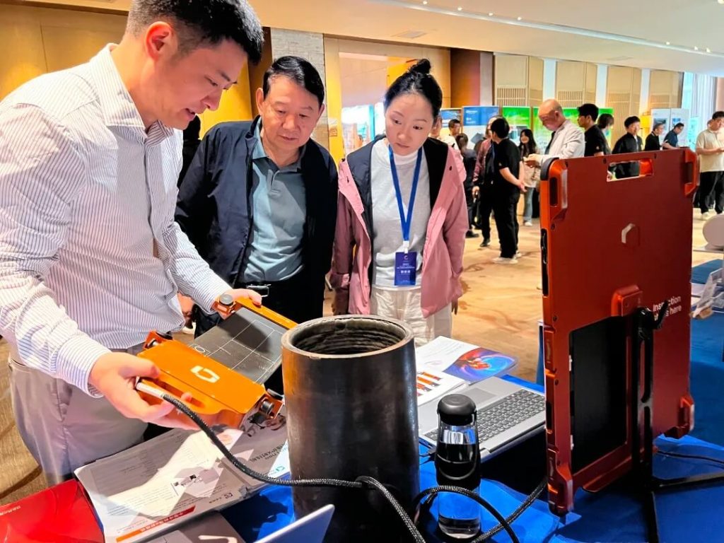 Waygate Technologies工程师在展会上向参观者演示DXR Flex探测器的操作方法,观众聚精会神观看设备检测管道样品。